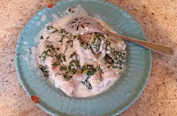 Catfish nuggets covered in a creamy sauce with shredded basil, on a blue serving plate.